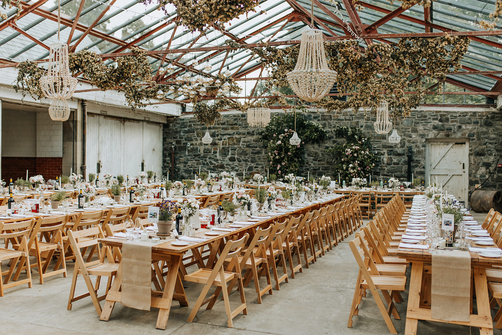 Réception de mariage en serre avec tables en bois et lustres suspendus